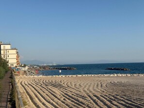 Une plage avec un ciel dégagé, une rive sablonneuse et un bâtiment doté de nombreux balcons.