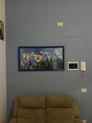 Une pièce avec un canapé beige, un tableau floral encadré, un thermostat et un téléphone fixé au mur.