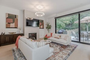 Un salon moderne avec un canapé blanc, une table basse et une cheminée. Une grande fenêtre offre une vue sur l’extérieur.