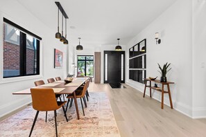 Un espace de salle à manger moderne avec une longue table, des chaises et des luminaires suspendus.