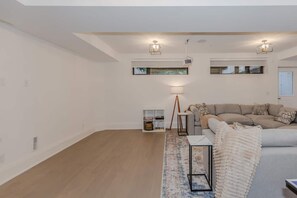 A modern living room with a sofa, a coffee table, and a floor lamp. - 5BD High Park Retreat w/ Home Theatre, Game Room & Deck (Toronto)