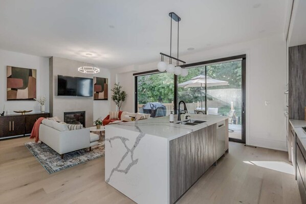 A modern kitchen with a large island, a dining area with a sofa, and a view of the outdoors. - 5BD High Park Retreat w/ Home Theatre, Game Room & Deck (Toronto)