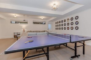 Une pièce avec une table de ping-pong, un canapé, une bibliothèque et des disques vinyle accrochés au mur.