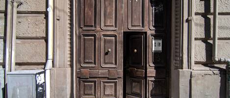 A wooden door with a traditional design, a small window, and a metal box on the ground.