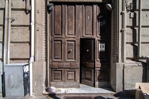 Eine Holztür mit traditionellem Design, ein kleines Fenster und eine Metallkiste auf dem Boden.