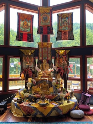 Una habitación con un ventanal grande, una estatua de Buda y diversos objetos religiosos sobre una mesa.