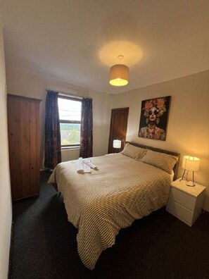 A bedroom with a bed, a nightstand, a window with curtains, and a painting on the wall. - Cheshire View 4 Beds House close to Wrexham City Centre (Summerhill)