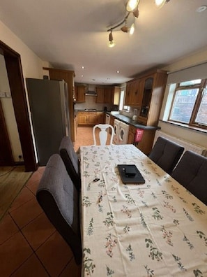 A dining area with a table set for two, a refrigerator, wooden cabinets, and a window with a view. - Cheshire View 4 Beds House close to Wrexham City Centre (Summerhill)
