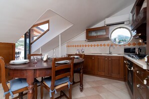 Eine Küche mit Holzausstattung, einem Esstisch mit Stühlen, einem Fenster und Blick ins Freie.