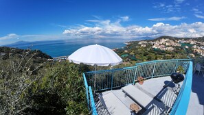 A balcony with a white umbrella, a blue railing, and a view of the sea and a coastal town. - Blue Paradise by Espresso Rentals (Massa Lubrense)