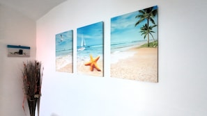 A wall with three framed beach scenes, a vase with dried plants, and a small shelf with a picture. - Blue Paradise by Espresso Rentals (Massa Lubrense)