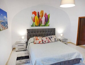 Ein Schlafzimmer mit einem Bett, zwei Nachttischen, einer Wandlampe und einem Gemälde von Tulpen.