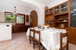 A dining area with a table set for four, surrounded by wooden cabinets and a tiled floor. - Essences of the Mediterranean by Espresso Rentals (Termini)