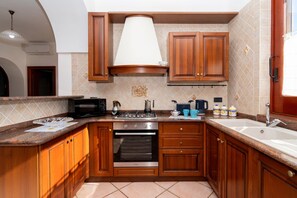 A kitchen with wooden cabinets, a stove, microwave, and a sink. - Essences of the Mediterranean by Espresso Rentals (Termini)