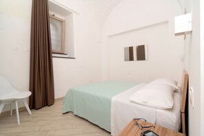A small, simple room with a bed, a chair, and a window with curtains. - Nonna Mary - Limone by Espresso Rentals (Sant'Agata Sui Due Golfi)