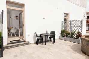 Een terras buiten met een tafel, stoelen, een glazen toegang en een witte muur.