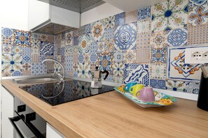 A kitchen with a modern stove, a sink, and a countertop with a tray of colorful cups. - Nonna Mary - Limone by Espresso Rentals (Sant'Agata Sui Due Golfi)
