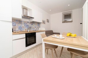 A modern kitchen with white cabinetry, a black oven, and a tiled backsplash. There is a dining table with chairs and a small window above it. - Nonna Mary - Ulivo by Espresso Rentals (Sant'Agata Sui Due Golfi)
