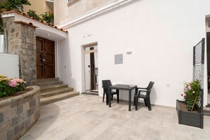 A courtyard with a stone wall, a wooden door, a white wall with a window, a table with chairs, and potted plants. - Nonna Mary - Ulivo by Espresso Rentals (Sant'Agata Sui Due Golfi)