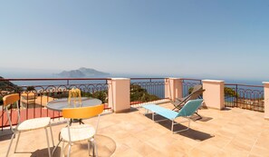 Eine Terrasse mit Tisch, Stühlen und Liegestühlen mit Blick auf die Küste.