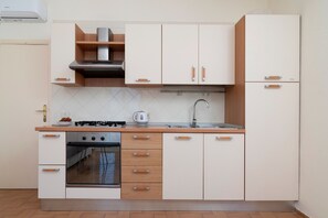 Cozinha compacta com armários brancos, fogão a gás, forno embutido e pia de aço inoxidável.