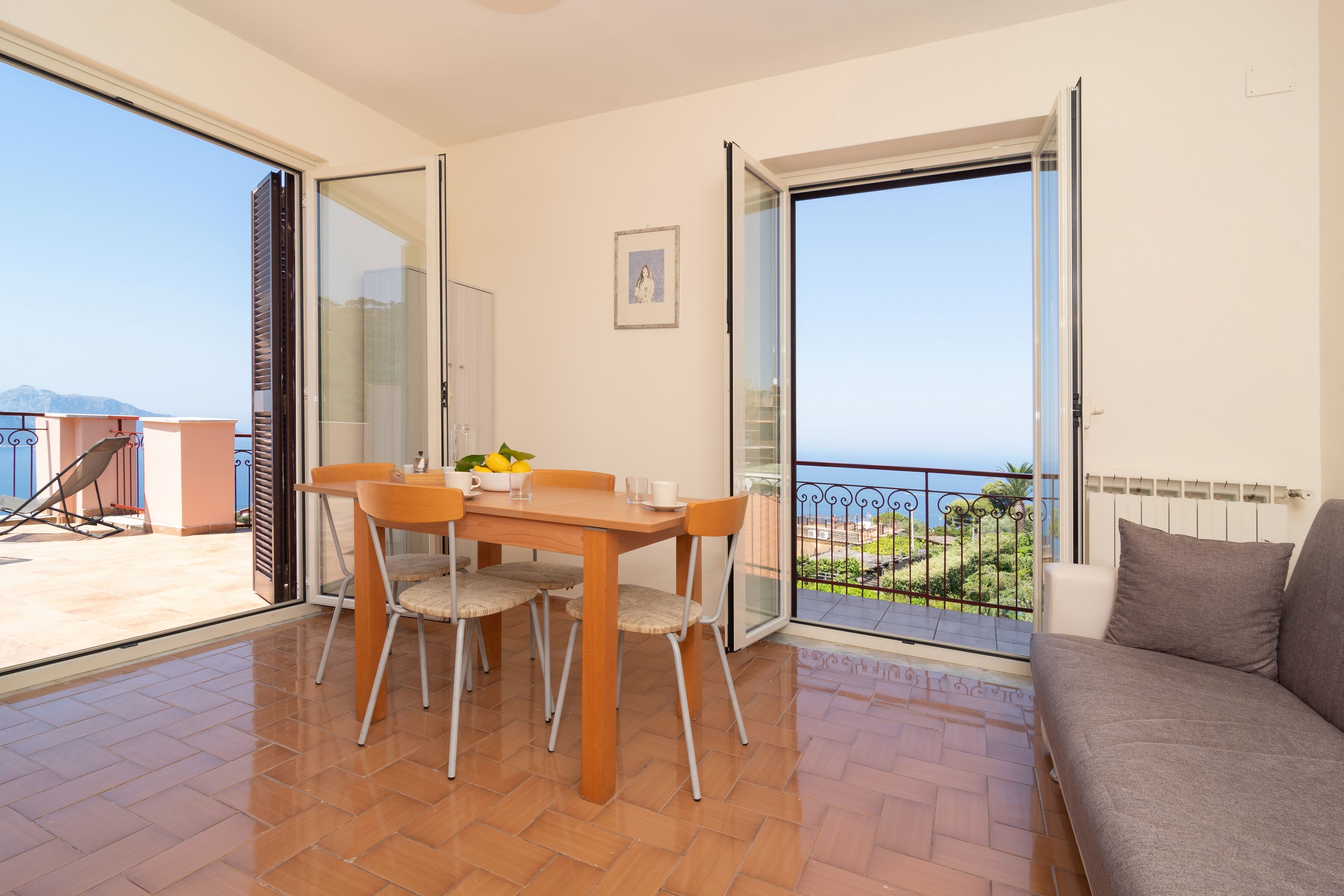 A balcony with a table and chairs, a sofa, and a view of the sea.