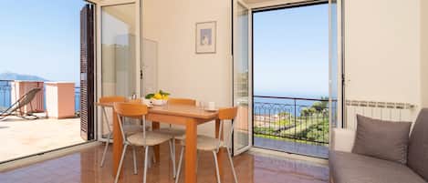 A balcony with a table and chairs, a sofa, and a view of the sea.