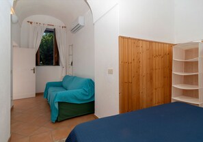 A bedroom with a bed, a green sofa, a wooden wardrobe, and a window with curtains. - Vitamin Sea by Espresso Rentals (Napoli)