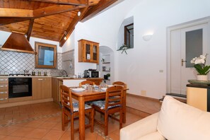 A compact kitchen with wooden cabinets, a dining table with chairs, and a small seating area with a sofa. - Vitamin Sea by Espresso Rentals (Napoli)
