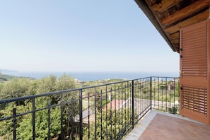 Ein Balkon mit Metallgeländer, der einen idyllischen Ausblick auf Bäume und den fernen Ozean bietet.