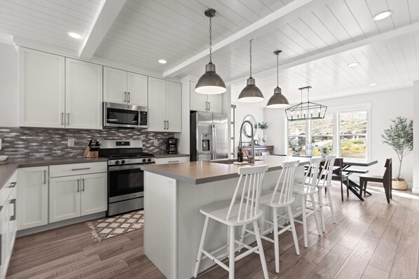 A modern kitchen with white cabinetry, stainless steel appliances, and pendant lighting. - Gone Ski Inn! Cozy Townhome Perfect for Families (Kamas)