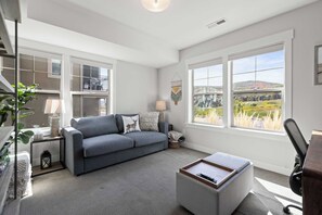 A modern living room with a grey sofa, a coffee table, and large windows offering a view of a green landscape. - Gone Ski Inn! Cozy Townhome Perfect for Families (Kamas)