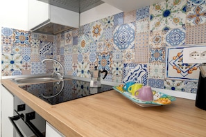 Een keuken met een moderne kookplaat, een spoelbak en een aanrecht met een dienblad kleurrijke kopjes.