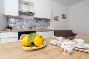 A modern kitchen with a dining area, featuring a fruit bowl with lemons, a coffee set, and a sofa. - Nonna Mary - Combo by Espresso Rentals (Sant'Agata Sui Due Golfi)
