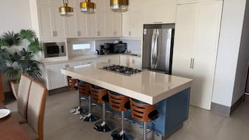 Una cocina moderna con una isla central, taburetes de bar, electrodomésticos de acero inoxidable e iluminación colgante.