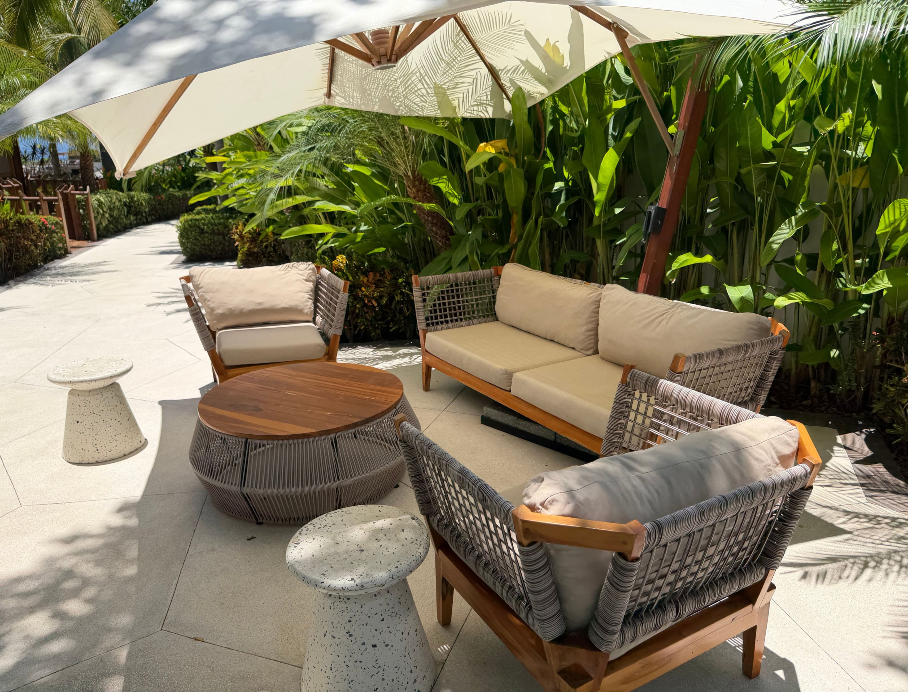 An outdoor seating area with wicker furniture, a round wooden table, and a white speckled stool.