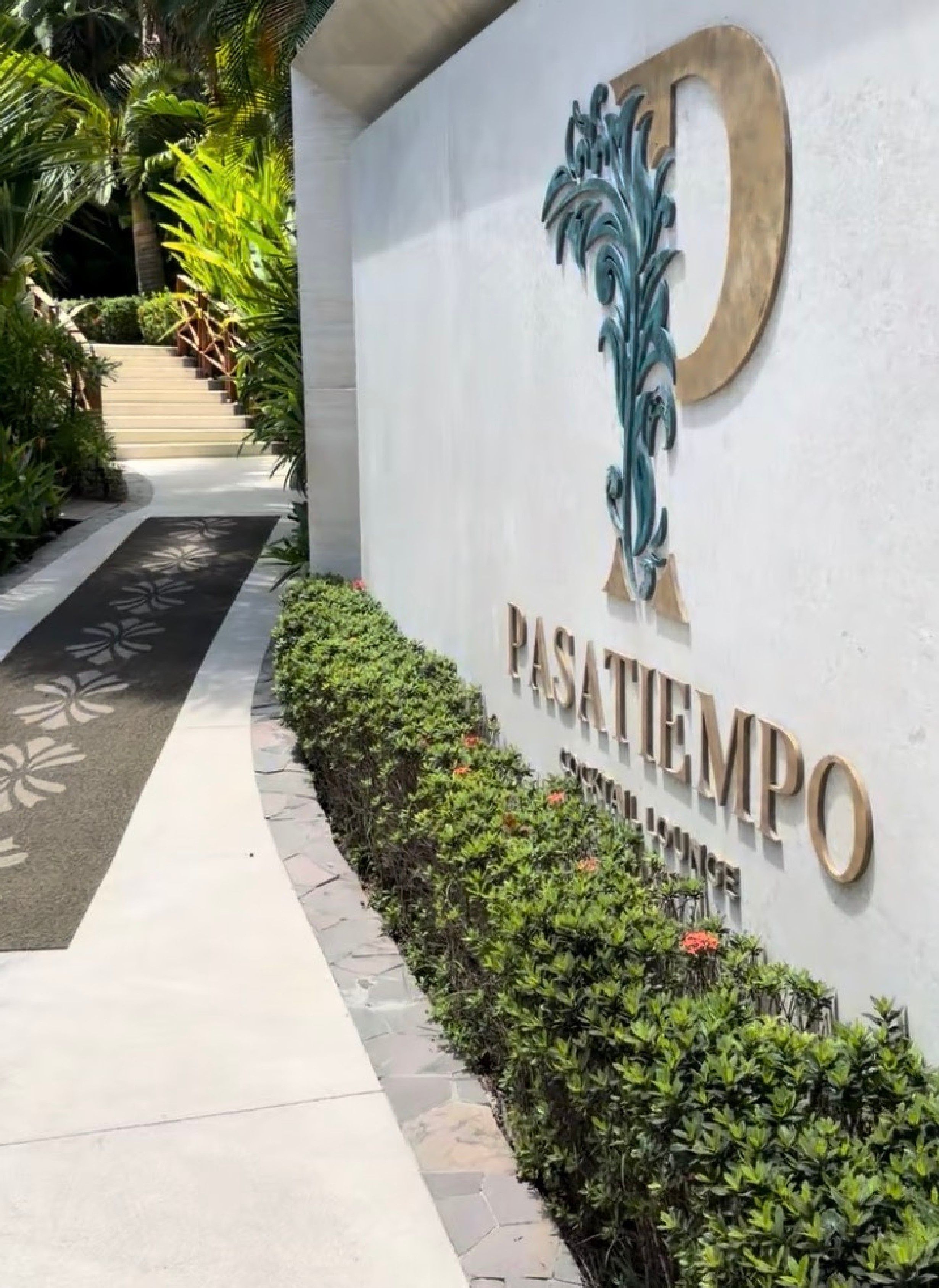 Señal para 'PASATIMPO' con un logotipo estilizado de la letra 'P', una escalera y un camino bordeado de follaje.