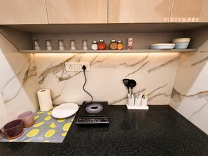 A kitchen with a marble countertop, a rice cooker, a set of utensils, and a shelf with jars. - Leafy Boho 1BHK in HSR Layout, near Koramangala,AC,WiFi (Bengaluru)