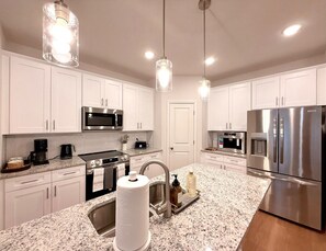 A modern kitchen with white cabinets, stainless steel appliances, granite countertops, and pendant lighting. - NEW - 8Beds 16People (Durham)
