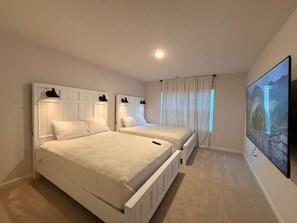 Ein Hotelzimmer mit zwei Betten, einem Flachbildfernseher und einem großen Fenster mit Vorhängen.