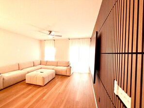 A modern living room with a sectional sofa, a ceiling fan, and a wooden accent wall. - NEW - 8Beds 16People (Durham)