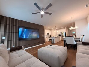 A modern living room with a flat-screen TV, a ceiling fan, and a dining area with a kitchen in the background. - NEW - 8Beds 16People (Durham)