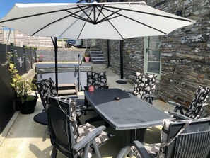 Eine Terrasse im Freien mit Tisch und Stühlen, einem großen Sonnenschirm und einer Steinmauer.