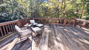 Eine Holzterrasse mit Korbmöbeln und einem Tisch, umgeben von Bäumen.