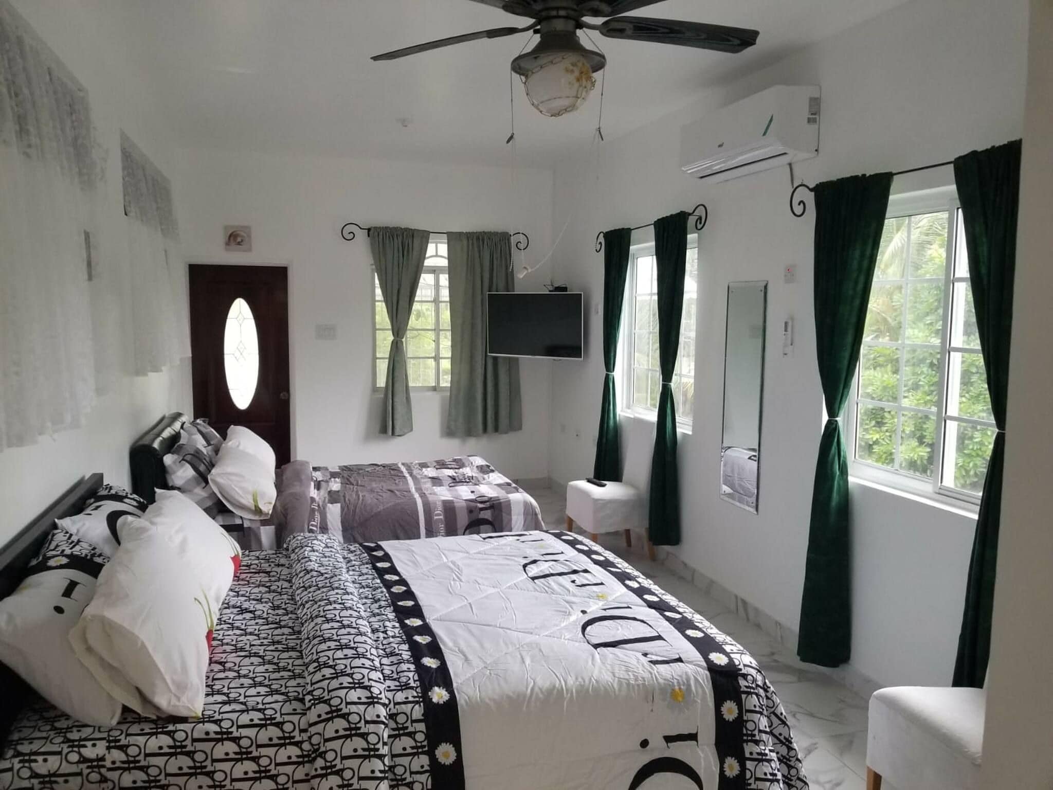 A bedroom with a bed, a television, a window with curtains, and a ceiling fan.