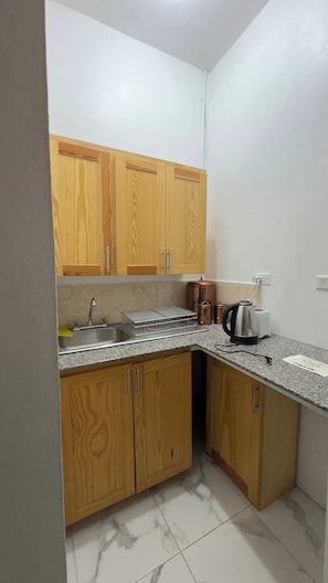 A compact kitchen with wooden cabinets, a stainless steel sink, and a countertop with a kettle and toaster. - Studio Flat Finished (Tollgate Clarendon Park)