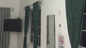 Ein Zimmer mit Wandairconditioner, einem an der Wand befestigten Fernseher, einem kleinen Tisch mit einer Tasse und einem Rauchverbotsschild.