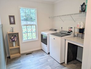 A laundry room with a washing machine, dryer, and a window with a floral pattern. - Cozy Carolina Farmhouse • Near Crowders Mtn & Belmont (Gastonia)
