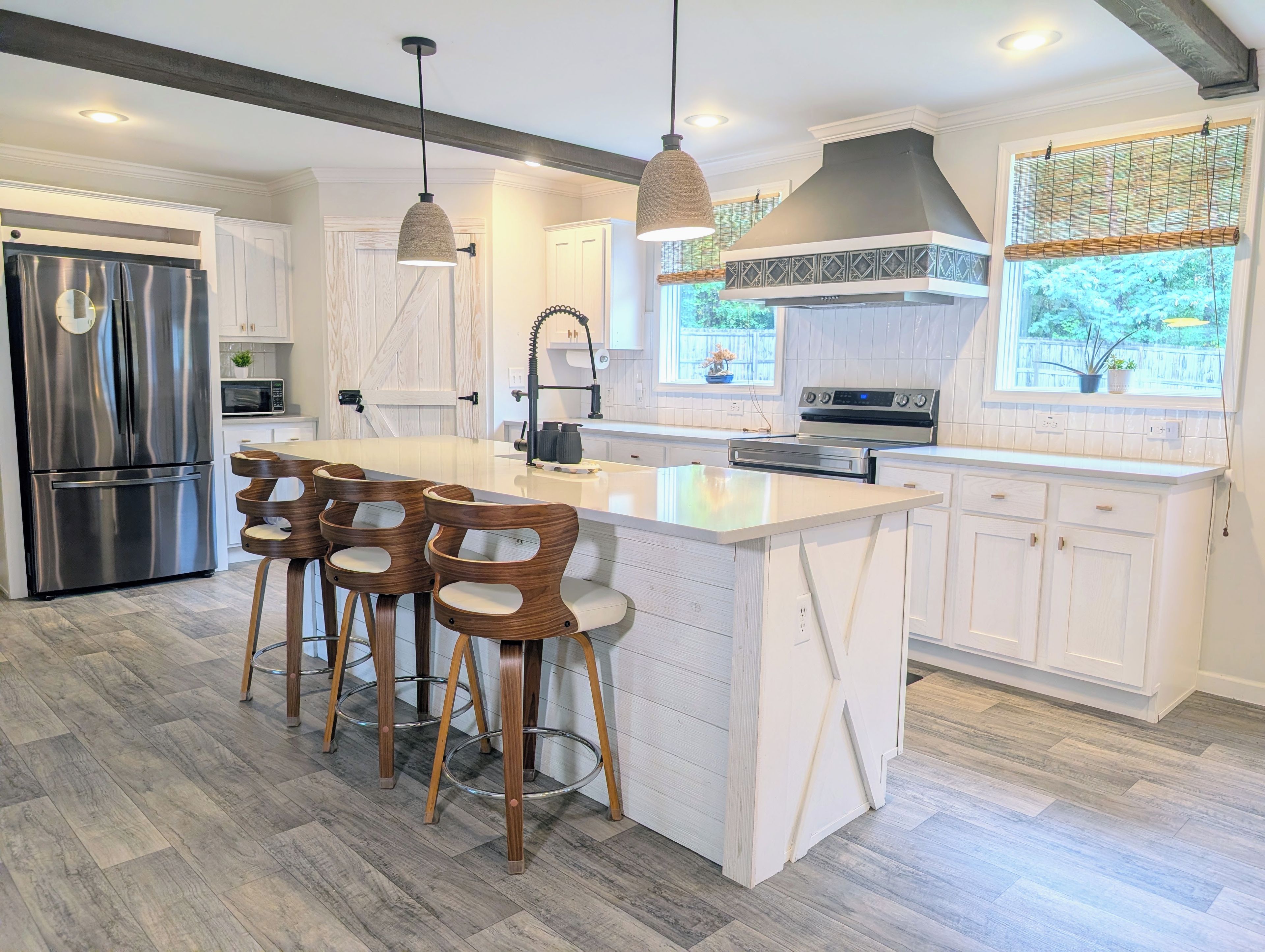 A modern kitchen with a central island, bar stools, stainless steel appliances, pendant lighting, and a view of the outdoors.