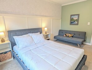 A bedroom with a large bed, bedside tables, a sofa, and a wall-mounted painting. - Cozy Carolina Farmhouse • Near Crowders Mtn & Belmont (Gastonia)